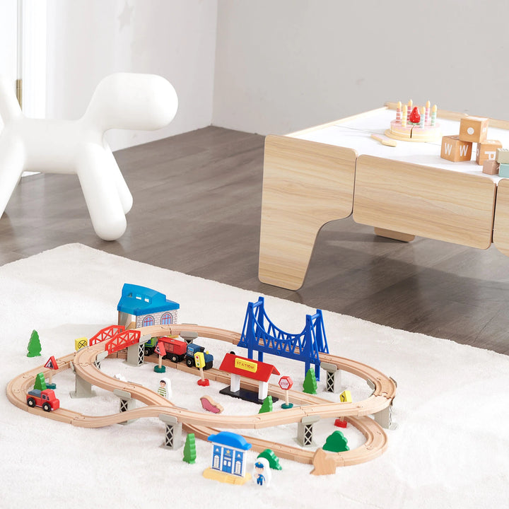 A wooden train set with a colorful locomotive, passenger cars, and cargo cars on a wooden track layout on a colorful rug.