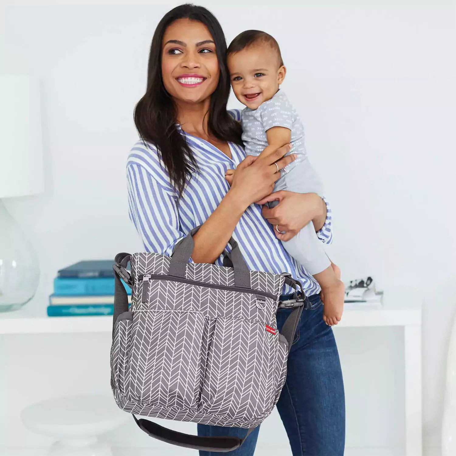 A smiling mum wearing a baby changing bag, holding her baby in her arms.