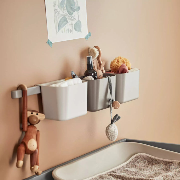 Image of a wall-mounted storage system for a baby's nursery, featuring two metal rails, three fabric bins, and four hooks. 