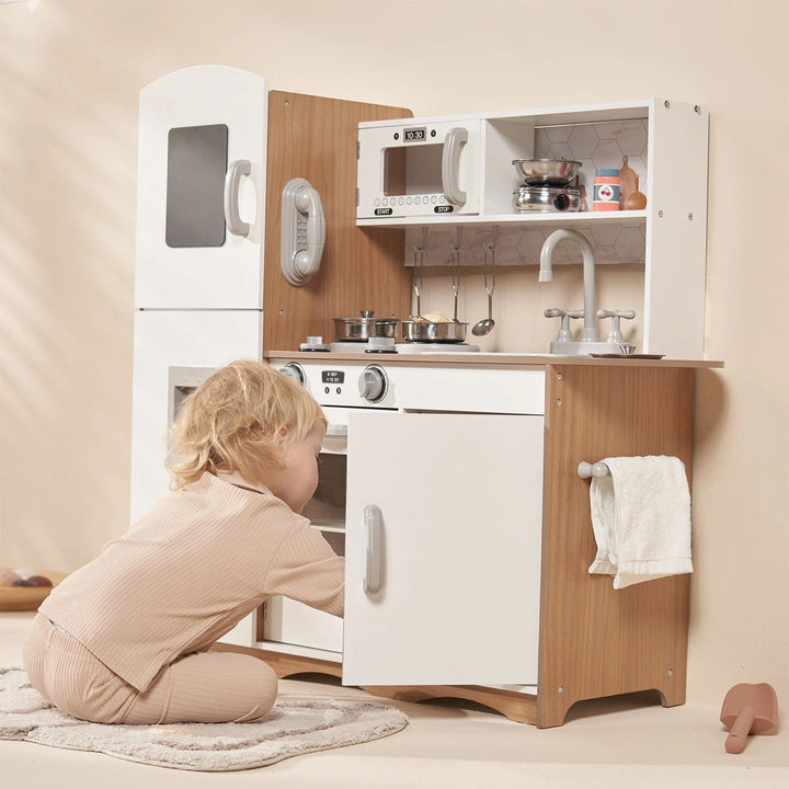 A child happily pretends to cook in their white wooden toy kitchen.