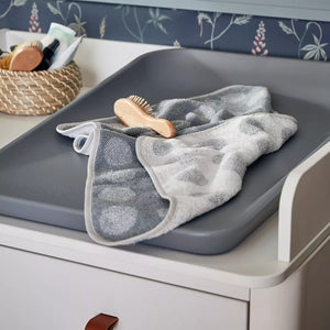 Close-up of the reversible changing pad topper, showcasing its soft texture and two color options. A baby lies peacefully on the topper during a diaper change