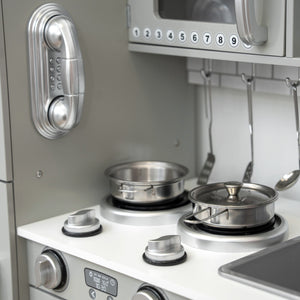 Stainless steel play kitchen setup with pots, pans, and utensils on a stove.