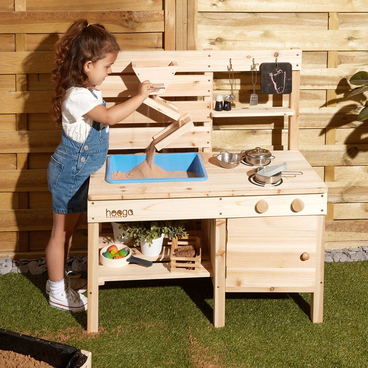 A girl is playing with the Hooga wooden mud kitchen sink.