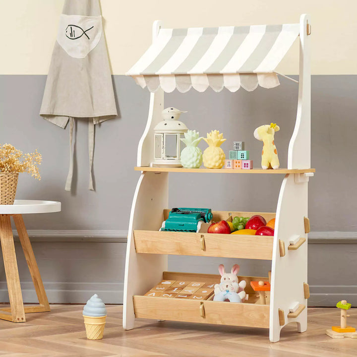 A wooden toy supermarket with a striped awning in a child's room. The shelf is filled with toys and a ice cream cone.