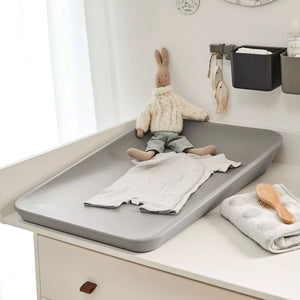 A Pearl grey, modern changing mat with raised edges and a smooth surface. It sits on a dresser in a stylish nursery.