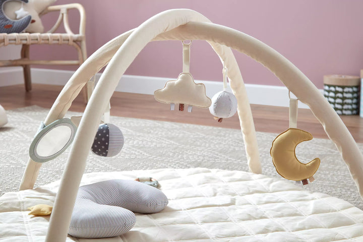 Baby play gym with cloud and moon toys on mat.
