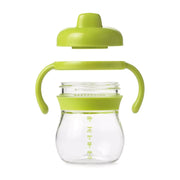 A green OXO Tot Transitions Spout Sippy Cup with a soft spout and removable handles. The cup is made of BPA-free plastic and has a capacity of 175 ml.