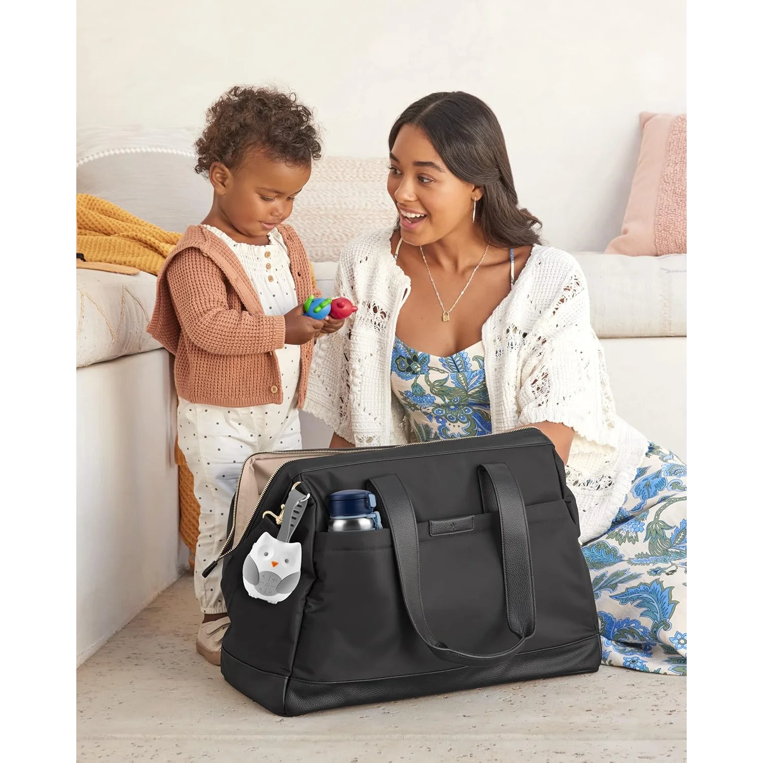 Woman and child interacting with a black diaper bag in a home setting