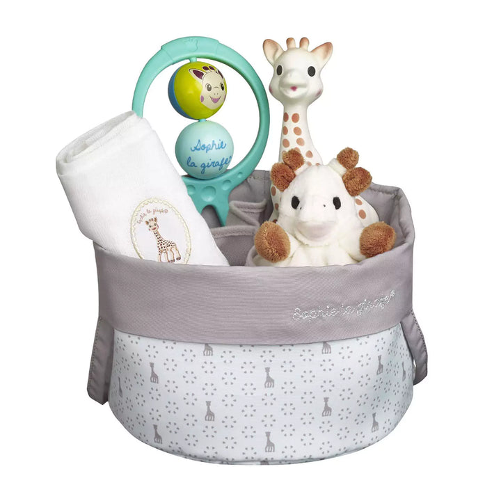 A woven basket filled with baby essentials and toys, including a Sophie la Giraffe teething toy, a plush elephant comforter with a pacifier holder, a muslin cloth, and a colorful swing rattle with bells