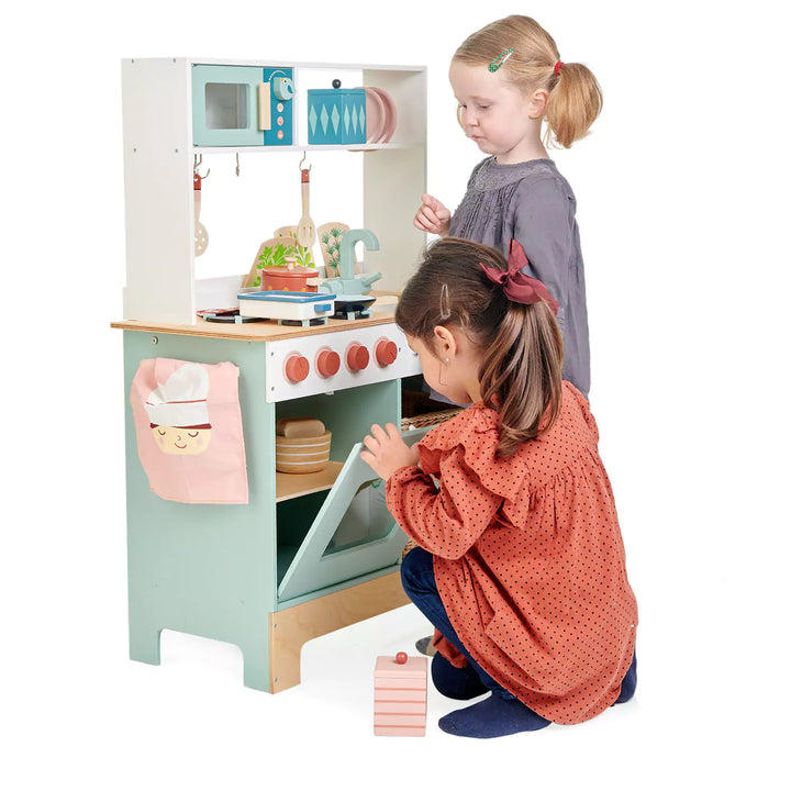 Two children engaged in pretend cooking at a wooden play kitchen, sharing utensils.