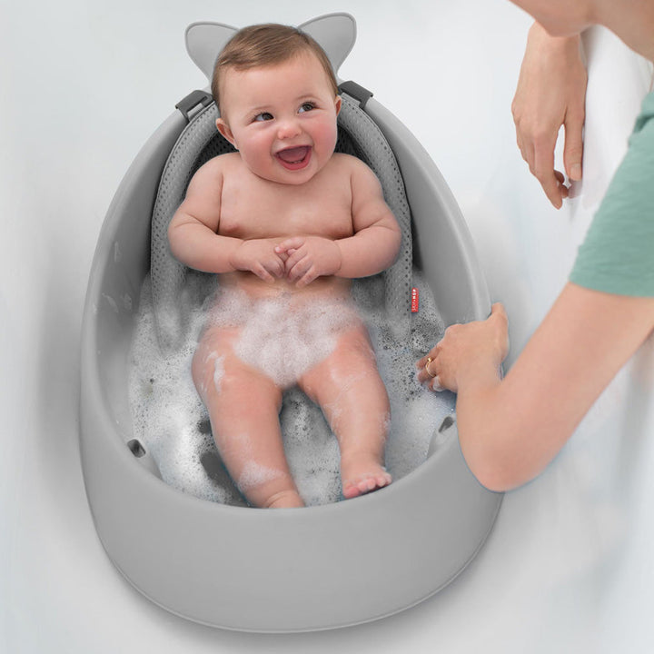 Baby smiling in a Skip Hop Moby 3-Stage Bathtub, supported by the removable sling.
