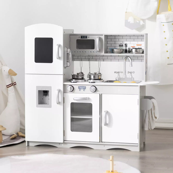 A grey wooden play kitchen with a refrigerator, stove, sink, microwave, and phone. The play kitchen has shelves and cabinets for storage. There is a duck in the background.